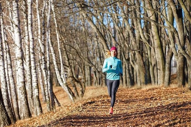 年轻的运动型女子在秋季公园跑步训练。美丽的健身女孩在寒冷的早晨慢跑