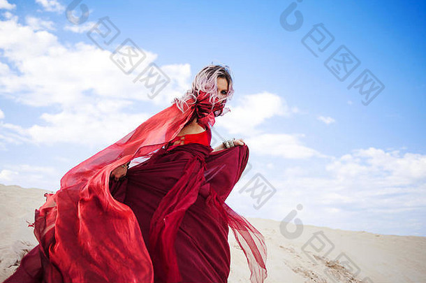 穿红衣服的女人。穿着令人惊艳的猩红色连衣裙的逃跑女孩。在户外，在沙漠里