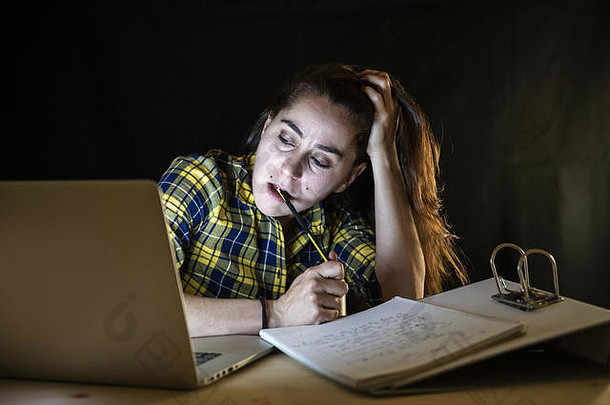 在一个为期末考试而学习的概念中，昨晚在笔记本电脑上工作的过度劳累的女学生试图不睡觉。