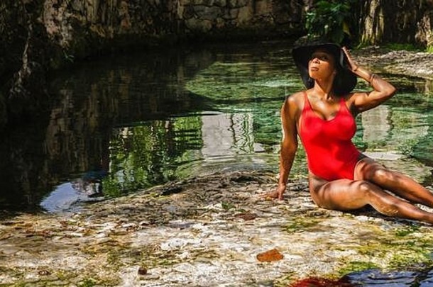 年龄在25岁至30岁之间的黑人妇女，穿着红色比基尼，享受着天然水源的<strong>清新</strong>，<strong>周</strong>围是热带自然