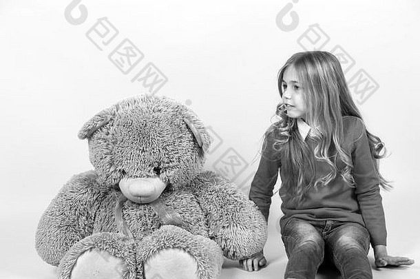 女孩和橙色背景的大泰迪熊坐在一起。带着灰色软玩具的孩子。节日、生日、周年庆典。带动物娃娃的孩子，礼物和礼物。快乐童年的概念。
