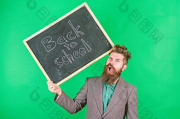 留胡子的老师拿着写有铭文的黑板回到学校的绿色背景。继续工作。头发蓬乱的老师对开学感到紧张。教授有压力的职业。