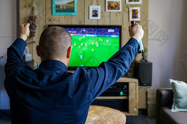 在家看一场重要的足球比赛。沙发上的男人正在为他最喜欢的球队欢呼