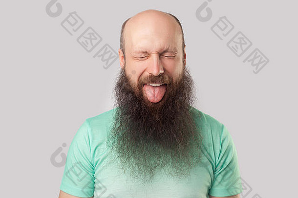 肖像有趣的中间岁的秃男人。长胡子光绿色t恤站关闭眼睛舌头室内工作室拍摄孤立的