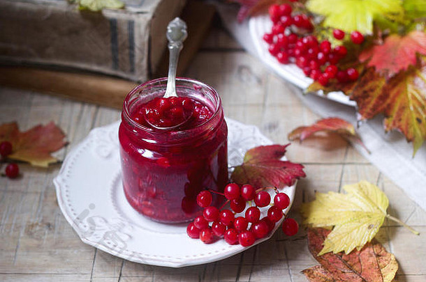 红色<strong>vi</strong>burnum浆果与糖和蜂蜜一起放在玻璃罐中，背景是书籍、浆果和树叶。
