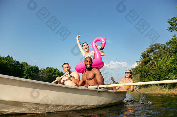 一群快乐的朋友在河里嬉笑和游泳。阳光明媚的河畔，穿着泳衣的快乐男女在船上。夏日、友谊、度假、周末概念。