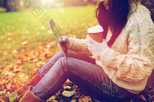 在秋天公园里，一位女士拿着平板电脑和咖啡