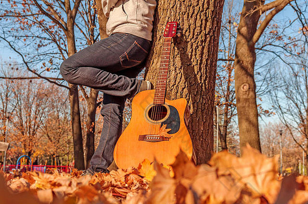 年轻的男人。坐着秋天公园吉他