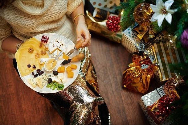 特写镜头年轻的家庭主妇黄金金片裙子白色毛衣装饰圣诞节树现在盒子吃奶酪持有盘