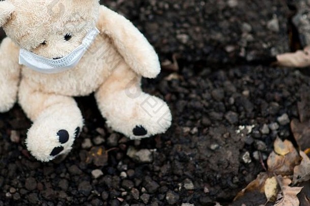 一只戴着医用面具的泰迪熊坐在肮脏的地面上，特写