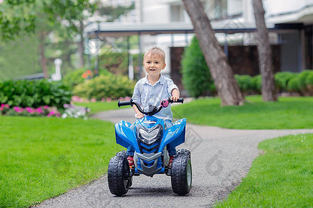 春夏时节，一个微笑的白人小男孩蹒跚学步，驾驶着蓝色电动汽车在外面的小路上行驶