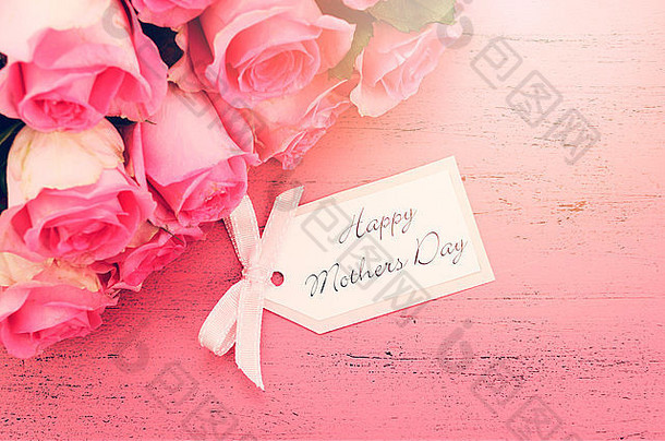 “母亲节快乐”粉红玫瑰位于复古风格的旧粉色木桌上，配有复古风格的滤光镜，并添加了日光灯