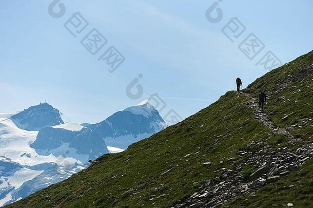 两名<strong>登山</strong>者背着背包，用<strong>登山杖</strong>在小路上行走，背景是美丽的山景。<strong>登山</strong>，人们在夏天到达顶峰。阿尔卑斯山的体育旅游。