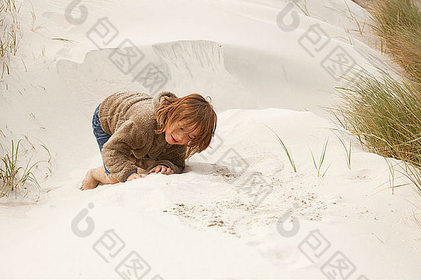男孩坐在沙丘上，在沙滩上玩耍