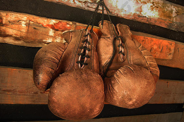 拳击手套挂在墙上。木墙上挂着一双老式皮革手套。红色和柔和的灯光。退役拳击手手套