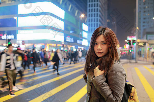 美丽的少女站在香港的夜景中，迷失在城市，繁忙的人群和黄色斑马线模糊的背景