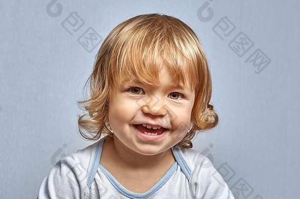 4岁左右的快乐金发白人微笑着摆姿势，在蓝色背景上为这幅肖像画拍照。