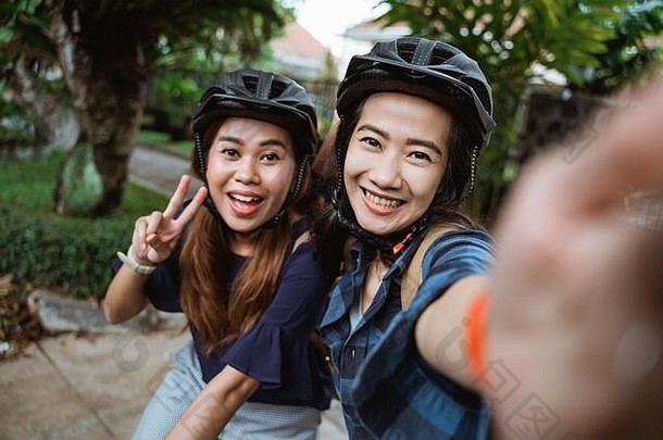 两名戴着头盔、背着照相智能手机的年轻女子在去校园前骑自行车时合影留念