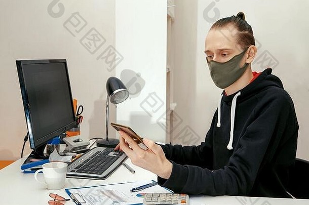 一位戴着防护面具的年轻专家在电脑前财务文件。冠状病毒，在防护面罩中工作。