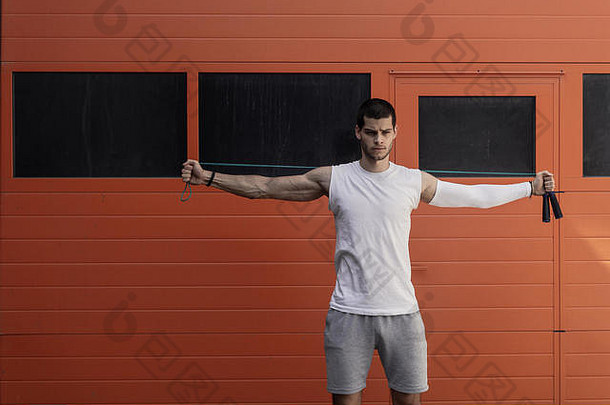 橙色墙壁背景上肌肉发达的年轻人用跳绳锻炼的肖像
