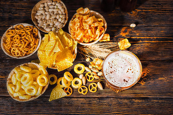 深色木桌上的盘子俯视图，盘子里放着啤酒、小麦、零散的坚果和椒盐卷饼。食品和饮料概念