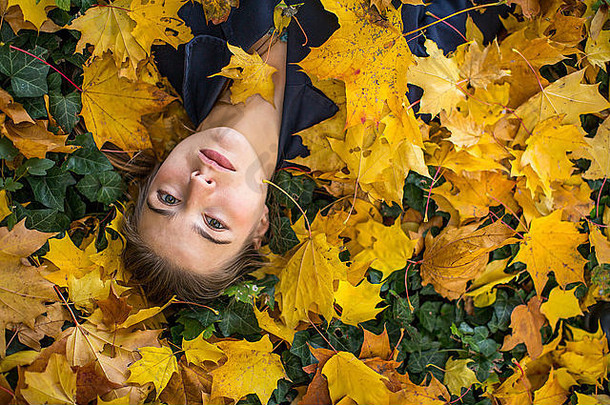 美丽的女孩躺在秋天公园的落叶里。