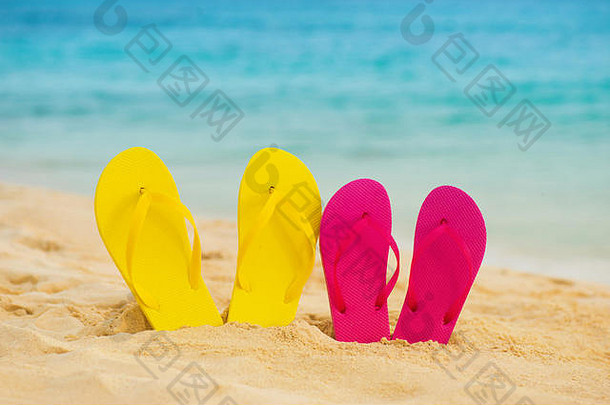 黄色和粉色的凉鞋站在沙滩上，背景是大海