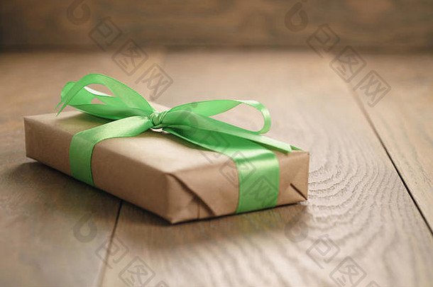 橡木桌上带绿色丝带蝴蝶结的棕色纸礼品盒