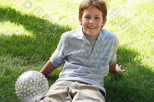 男孩球坐着公园草坪上肖像