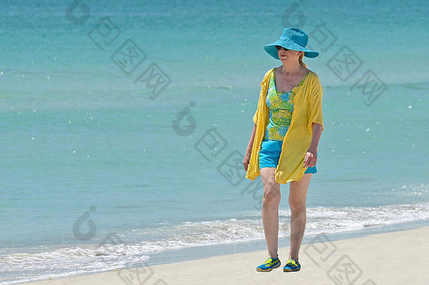 穿着非常时髦的衣服在海滩上散步的迷人的成熟女人