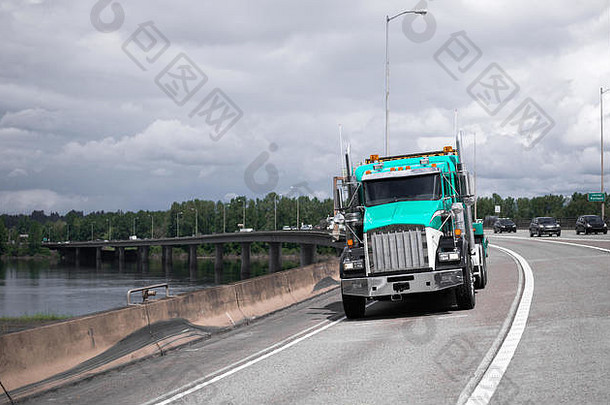 一辆大型绿色半卡车正行驶在一条宽阔的州际公路的右车道上，这条公路在哥伦比亚河的混凝土支架<strong>上架</strong>起了一座相当长的桥梁