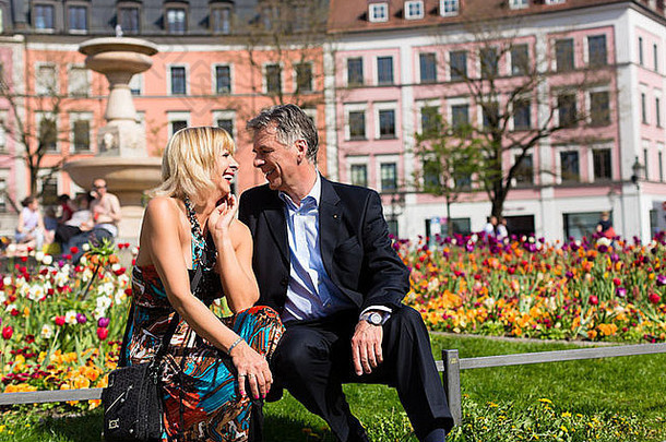 成熟的高级夫妇坐着板凳上春天城市享受太阳
