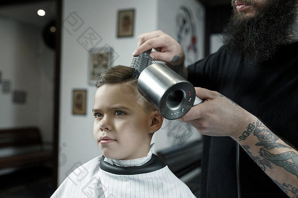 <strong>儿童</strong>理发师在黑暗的背景下给小男孩理发。心满意足的可爱学龄前男孩正在理发。
