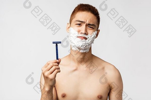 美人卫生概念不情愿的不高兴亚洲男人。不愿刮胡子失望相机扮鬼脸显示剃须刀