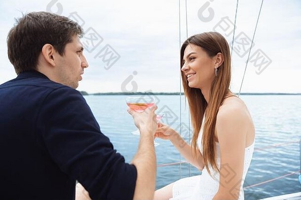 一对幸福微笑的夫妇在户外的船上聚会上喝着<strong>伏</strong>特加鸡尾酒，欢快而快乐。年轻人享受海游、青春和<strong>暑</strong>假的乐趣。酒精，假期，休息，爱。