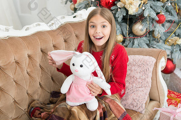 这是难以置信的。小女孩和可爱的兔子在圣诞树旁。小孩带着礼物开心地笑着。小女孩抱着兔子<strong>玩具</strong>。小孩玩软<strong>玩具</strong>。最好的圣诞<strong>玩具</strong>。