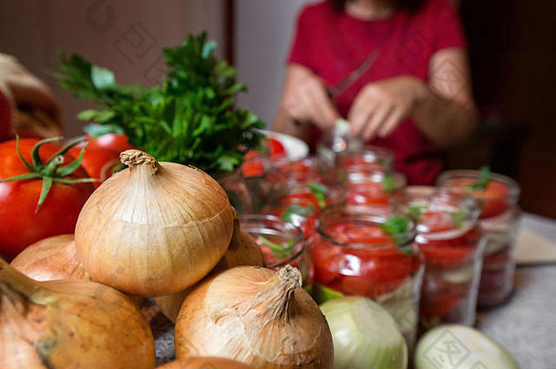 将新鲜西红柿和洋葱放入果冻腌汁中罐装。女人用手把红色成熟的番茄片和洋葱圈放进罐子里。罗勒，欧芹叶在上面
