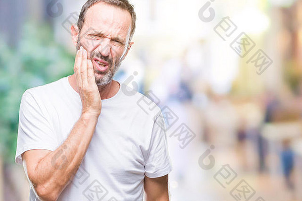 中年白发老人，穿着白色t恤衫，隔着孤立的背景，用手触摸嘴巴，因为牙痛或脱毛而表情痛苦