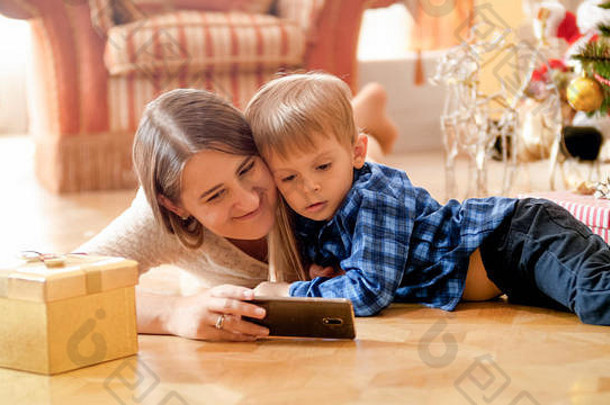 圣诞节早上，一个蹒跚学步的小男孩和妈妈在电话里看动画片