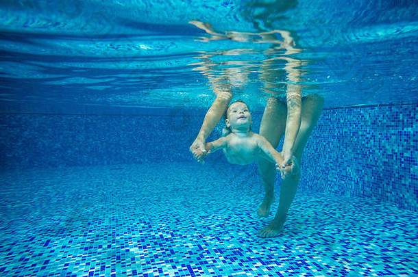 小男孩在室内游泳池水下游泳，妈妈或老师牵着他的手