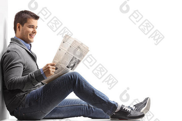 年轻人坐在地板上看报纸，靠在白色背景上的隔离<strong>墙</strong>上