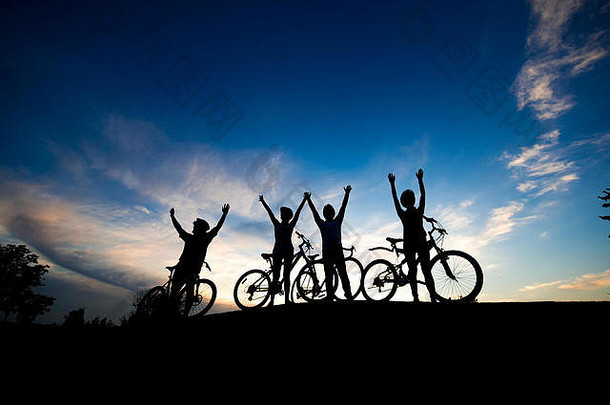 日落时，四名自行车手举起手。