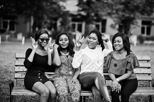 四个非洲裔美国女孩坐在户外的长椅上，双手举在空中。