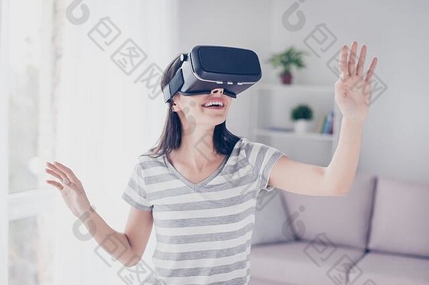 在虚拟现实中，戴着虚拟现实耳机的美丽、可爱、兴奋的女人抬头并试图触摸物体