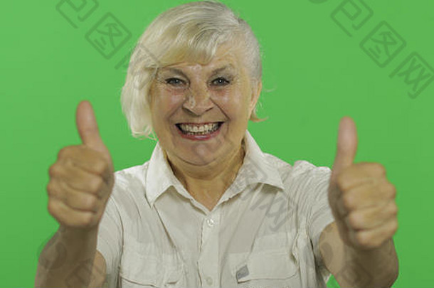 一位老妇人竖起大拇指微笑着。穿着白衬衫的漂亮老奶奶。放置您的徽标或文字。色度键。绿色屏幕背景