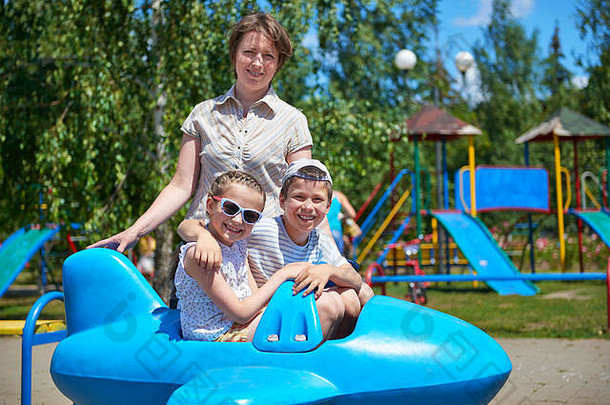 儿童和妇女在城市公园的蓝色飞机上飞行，快乐家庭概念，暑假