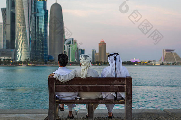 <strong>卡塔尔</strong>多哈，三名身着传统服饰的阿拉伯人坐在长凳上，眺望阿拉伯海湾