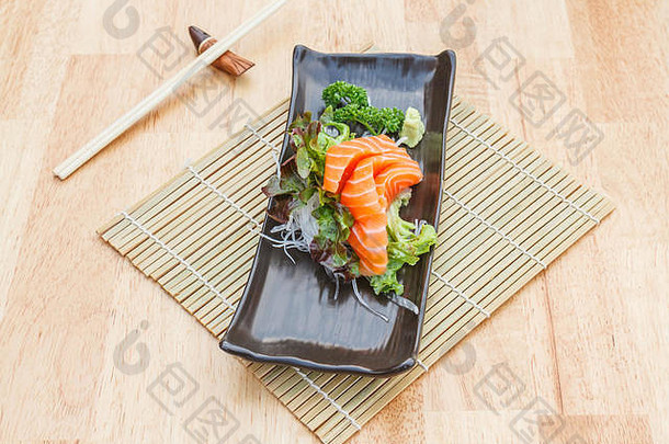 生鱼片大马哈鱼蔬菜萝卜黑色的板筷子木表格