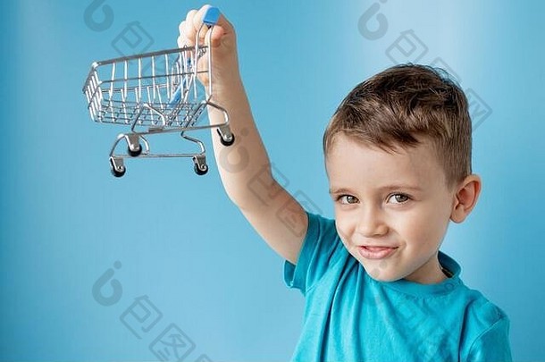 穿着蓝色t恤衫的男孩手里拿着购物车，蓝色背景上的商品。购物和销售概念
