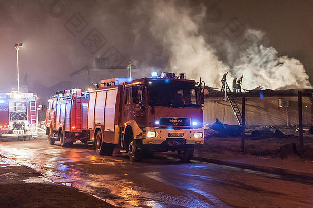 在寒冷的冬夜，波兰消防车在灭火，消防员在冒烟的屋顶上行走